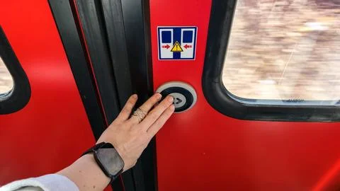  Hand pressing circular door button on bright red train carriage during c.. Stock Photos