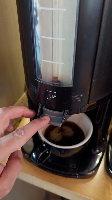 Hand pressing coffee dispenser while cup fills beneath black kitchen machine Stock Footage 345122998