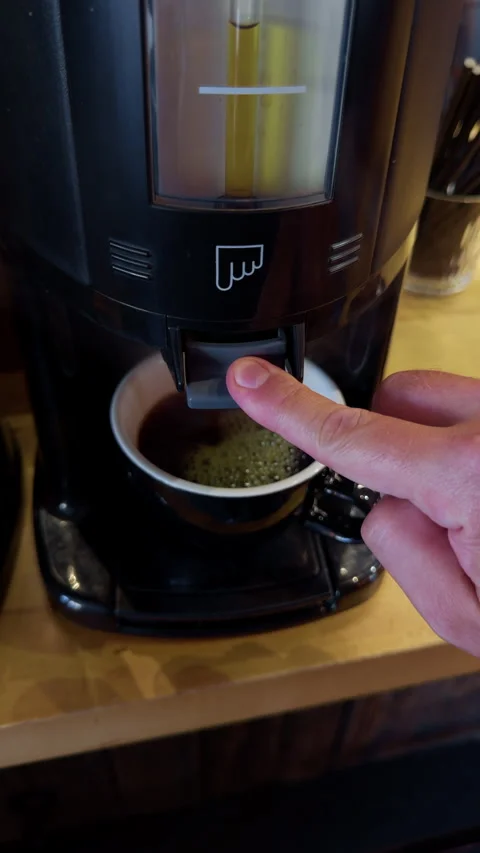 Hand pressing coffee machine dispenser above cup with foam on wooden countertop Stock Footage 344966779