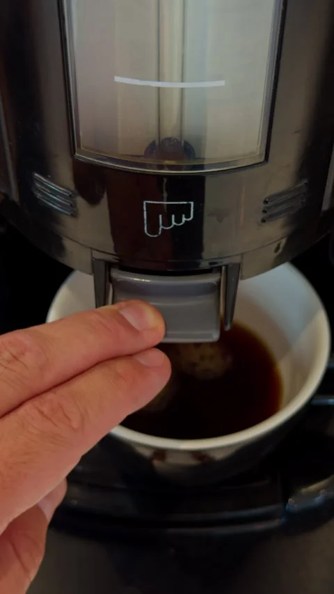 Hand pressing coffee machine dispenser with cup below, close-up of home brewing Stock Footage 345452969