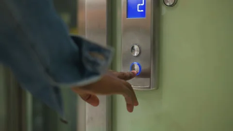 Hand pressing elevator button with illuminated blue arrow indicating upward Stock Footage 316649514