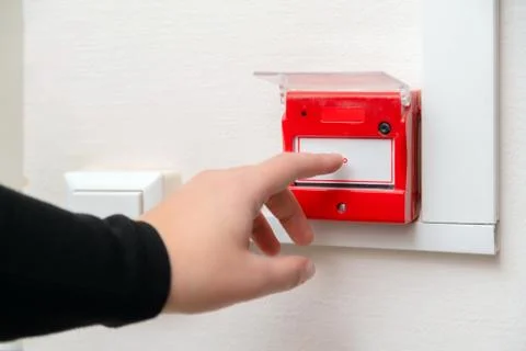 Hand pressing fire alarm button at school or business office. Close up Photos