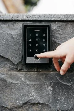 Hand pressing keypad on a modern intercom system mounted on a stone wall, s.. Stock Photos