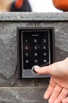 Hand pressing keypad on modern security system with sleek design and stone .. Stock Photos