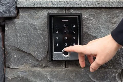 Hand pressing keypad on modern security system mounted on stone wall with s.. Stock Photos