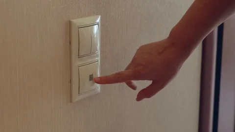 Hand pressing light switch on beige wall, turning on electricity indoors Stock Footage 318774709