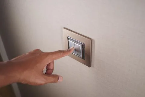 Hand pressing a light switch in a simple room Stock Photos