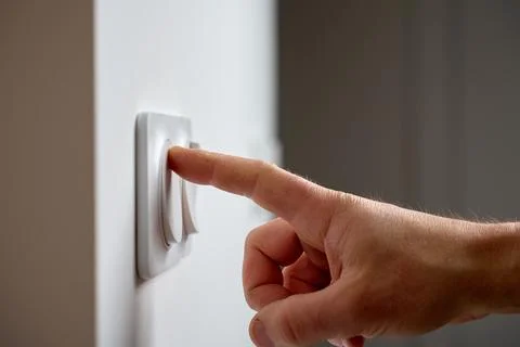 Hand pressing light switch to turn on lighting Stock Photos