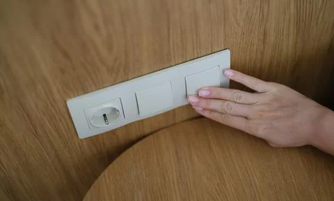 Hand pressing light switch in wall of house closeup Stock Photos