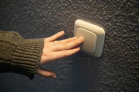 Hand pressing light switch on wall. Stock Photos