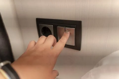 Hand Pressing Modern Light Switch Beside Electrical Wall Outlet Stock Photos