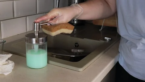 Hand pressing a pump dispenser bottle to release liquid dish soap onto a ye.. Stock Footage 320737704