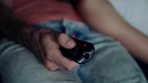 Hand pressing on the remote control button, switching channels, sitting on .. Video stock 257873546