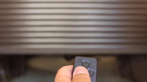 Hand pressing remote control button to open an automated garage door with a Stock Footage 340351565