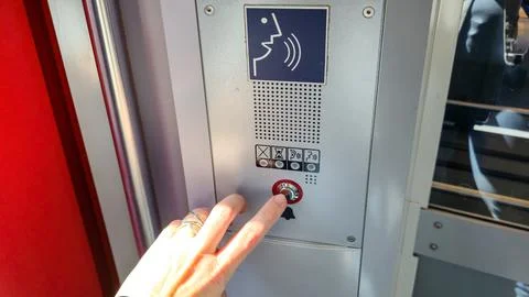  Hand pressing silver button on metal intercom panel inside bright public. Stock Photos