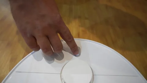 Hand Pressing Start Button on Robotic Vacuum Cleaner Stock Footage 321946466