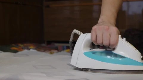 Hand pressing steam iron across patterned bed sheet Stock Footage 342863579