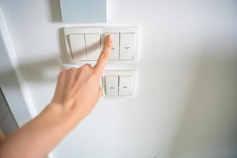 Hand pressing wall light switch in modern home interior. Energy saving and smart Stock Photos