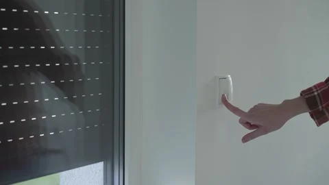 Hand pressing a wall switch to control electric window blinds in a modern home Stock Footage 303310061