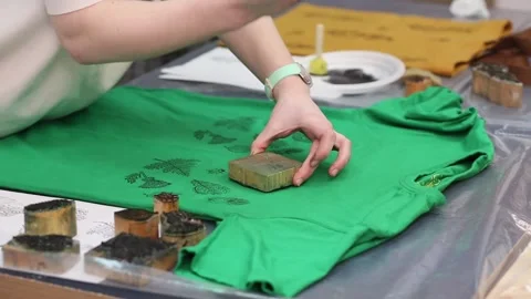 Hand-printed pattern on fabric. Women's hands put a seal on a green T-shirt with Stock Footage 170478456