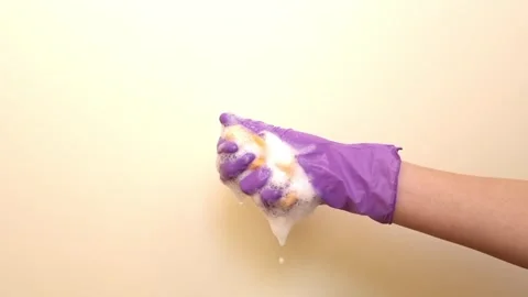 A hand in a protective glove squeezes foam out of a sponge Stock Footage 335203648