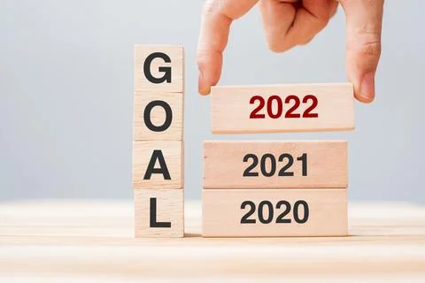 Hand pulling 2022 block over 2021 and 2020 wooden building on table backgroun Fotos de archivo