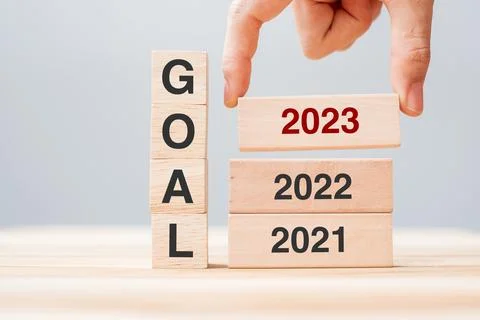 Hand pulling 2023 block over 2022 and 2021 wooden building on table backgroun Fotos de archivo