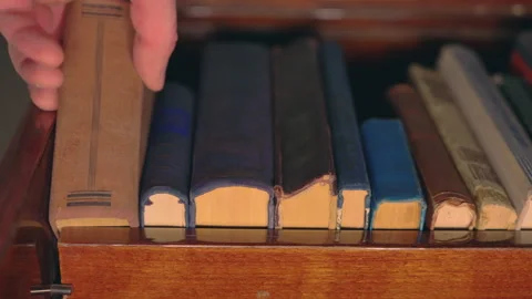 Hand Pulling Antique Book from Wooden Shelf: Low-Angle Close-Up View | Vintage Stock Footage 340939403