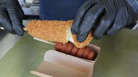 Hand pulling apart a delicious, crispy Korean cheese corn dog, showing the melte Stock Footage 331955979