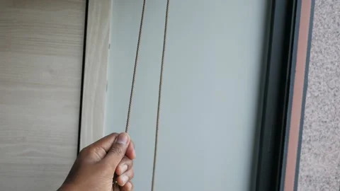 Hand pulling blind cord down to cover window for privacy in home office or .. Stock Footage 332579007
