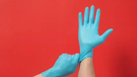Hand is pulling blue latex gloves or surgical gloves on red background. Stock Photos