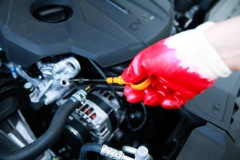 Hand pulling a car's dipstick using a red glove. Checking engine oil Stock Photos