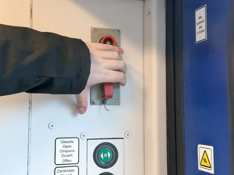 Hand pulling emergency lever on train door control panel, indicating safety.. Stock Photos