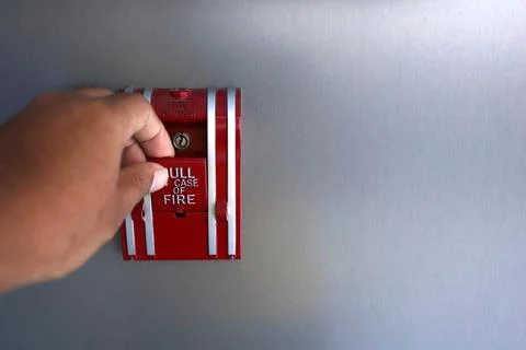 The hand is pulling the fire alarm on the wall. Fire alarm switch in the buil Stockfoto's