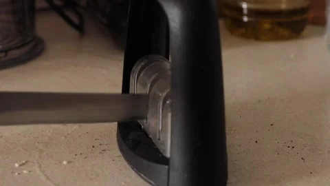 Hand pulling a kitchen knife through a manual sharpening tool on a countert.. Stock Footage 320738616