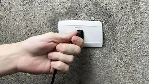 A hand pulling the plug out of an outlet Stock Photos