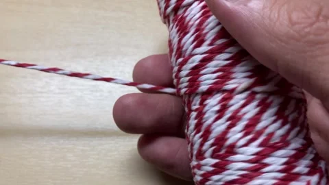 Hand pulling red and white twine thread close up shot on wooden table. Video stock 248205375