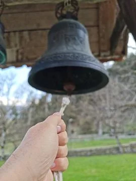 Hand pulling rope to ring old bell in natural environment Stock Photos
