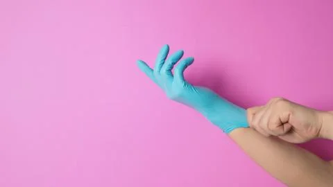 Hand is pulling rubber gloves or blue latex glove on pink background. Stock Photos