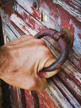 Hand pulling rusty handle on old wooden door with peeling paint, close-up Stock Photos