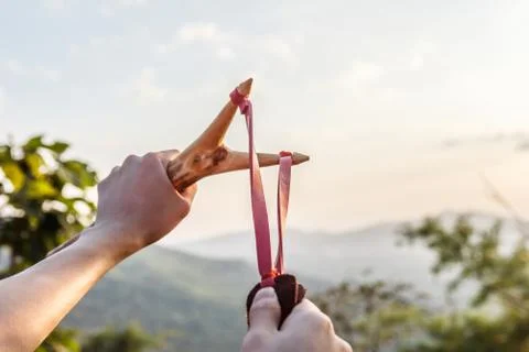 Hand pulling slingshot to shoot tree seed into forest. Stock Photos