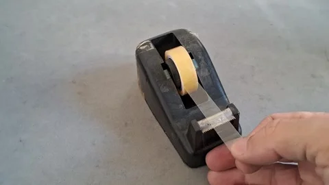 Hand pulling sticky clear tape from black heavy desk dispenser footage Stock Footage 339247420