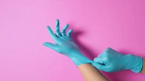 Hand is pulling surgical gloves or blue latex gloves on pink background. Stock Photos