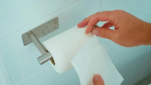 Hand pulling white toilet paper from metal wall holder in public restroom. Close Stock Footage 345125787