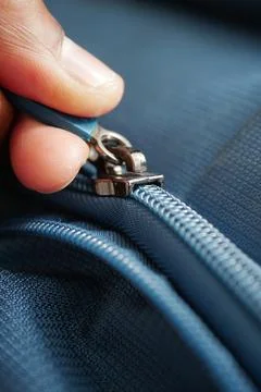 Hand pulling a zipper on a blue fabric item Stock Photos