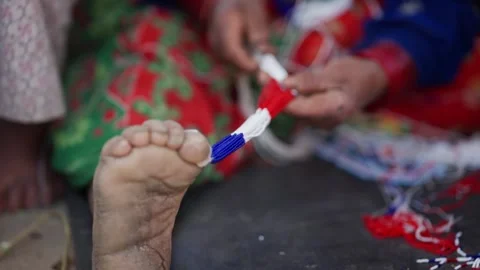 Hand pulls bead thread anchored by foot during necklace weaving Stock-Footage 342399171