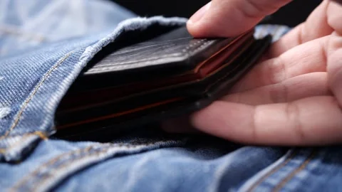 Hand pulls a black wallet out of the pocket of a blue denim jacket Stockbeeldmateriaal 144227072