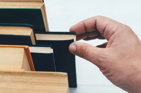 Hand pulls a book, from the bookcase. Stock Photos