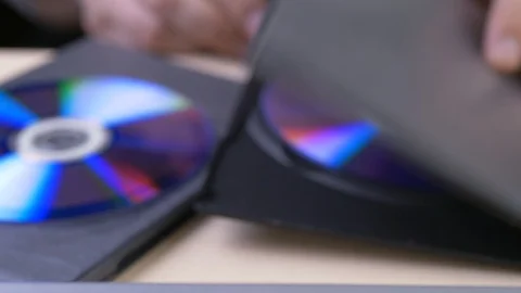 The hand pulls the disc from the box and insert to dvd player Stock Footage 103680782