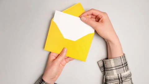 A hand pulls out a white card from a bright yellow envelope. Top view of yellow Stock Footage 269542306